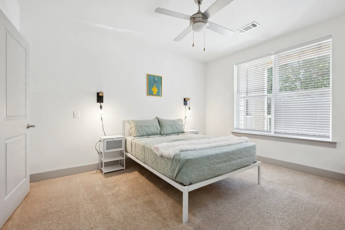 A serene bedroom featuring a comfortable bed with plush linens, a nightstand, eye-catching artwork, and a window letting in soft natural light. The atmosphere is peaceful, ideal for relaxation and quiet moments.