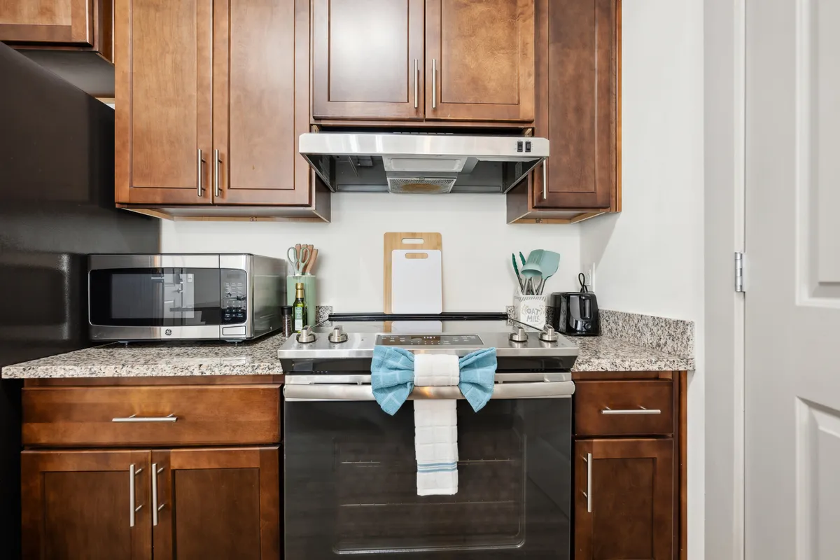 A warm, inviting kitchen scene featuring a stainless steel oven, granite countertop, rich wooden cabinets, and colorful kitchen utensils neatly arranged. The atmosphere is homely and bustling, perfect for culinary creativity or gathering with loved ones.