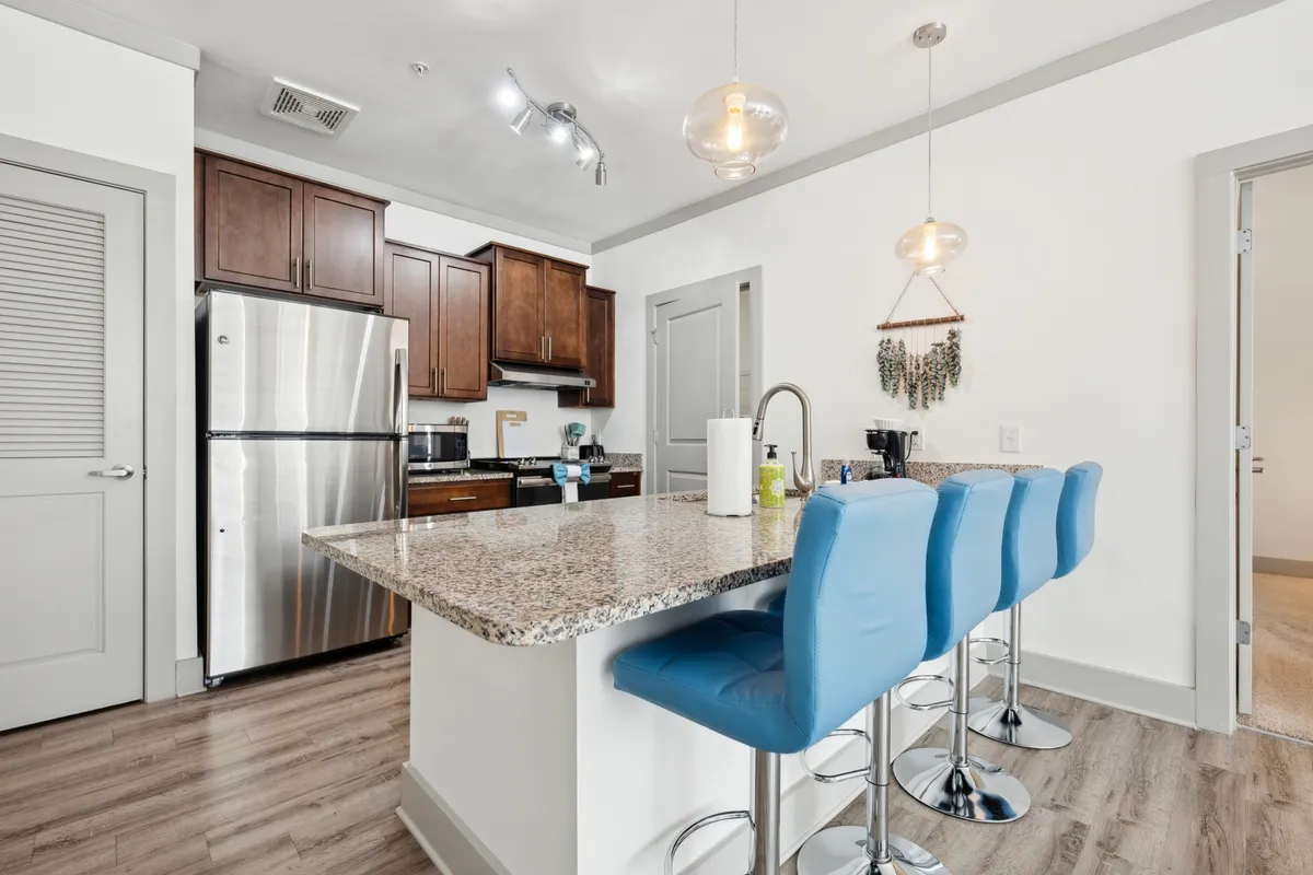A bright, modern kitchen featuring a striking granite countertop, three cheerful blue bar stools tucked under the breakfast bar, and gleaming stainless steel appliances. The space is open and inviting, accented by thoughtful decor touches that enhance its contemporary vibe.