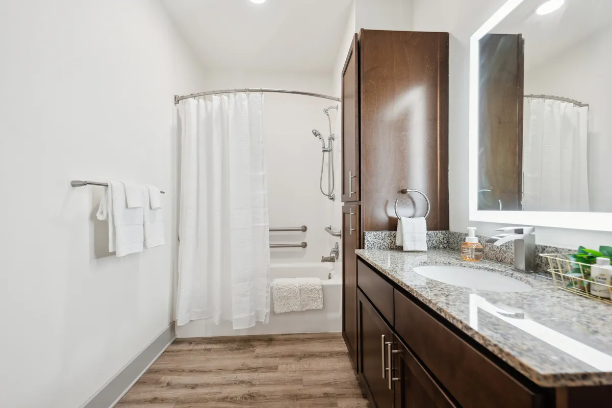 A modern bathroom with a granite countertop vanity, illuminated mirror, and a shower area with a soft curtain. The space feels fresh and calming, ideal for self-care routines and unwinding after a busy day.