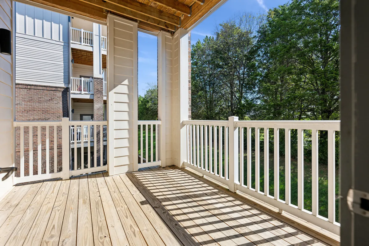 This image showcases a charming exterior wooden deck with white railings, surrounded by green trees. The setting is calming and features a table and chairs, perfect for enjoying coffee together or reading in the morning light. The deck offers opportunities for sunrise views and stargazing, enhancing the sense of retreat and intimacy.