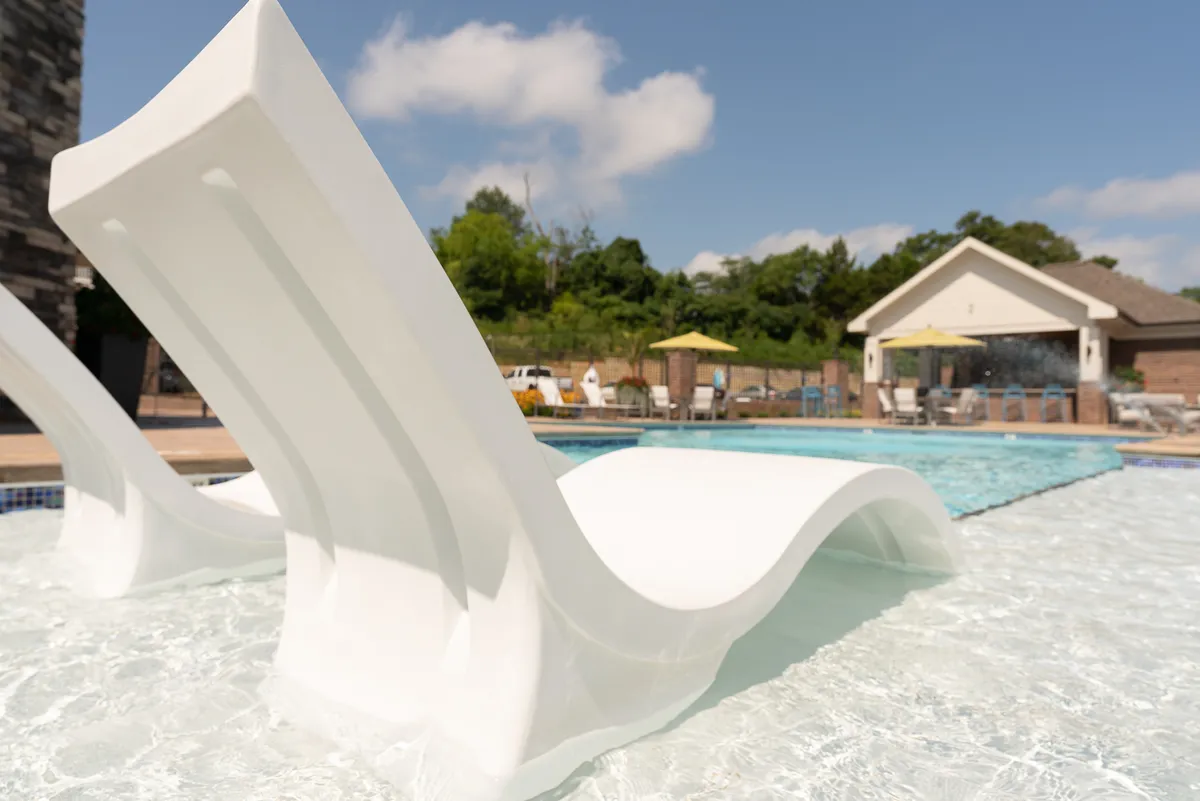 This exterior image features a sparkling swimming pool surrounded by comfortable pool loungers and shaded by sun umbrellas. The area is inviting, with a relaxing ambiance that offers an appealing escape for both relaxation and low-key socializing. The pool area is bathed in natural light, hinting at opportunities for leisure and unwinding after work.