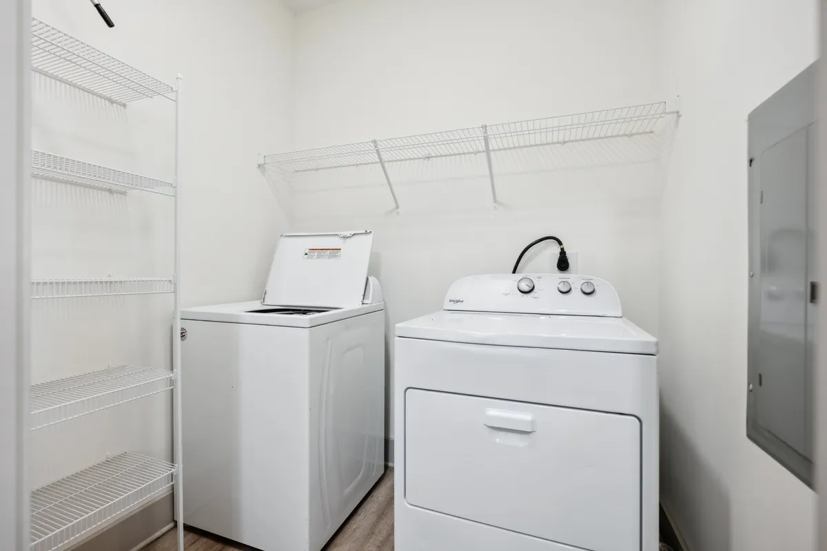 A practical laundry area inside the apartment, complete with a washing machine, dryer, and neatly organized shelving for supplies. The space is clean and efficiently designed for daily living convenience.